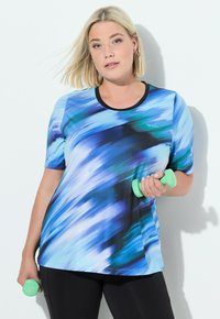 Camisa deportiva azul y negra de manga corta, con un patrón abstracto ondulado, escote redondo y logo en el pecho, combinada con pantalones negros y mancuernas verdes.