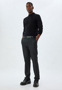 Schwarzer Rollkragensweater, schmale schwarze Hose und schwarze Schuhe. Getragen mit einem schwarzen Gürtel, glatter Textur und schlankem Design.