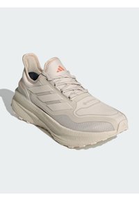 Light gray athletic shoe with textured mesh upper, reinforced toe, and three-stripe design. Features a cushioned sole and lace-up closure.