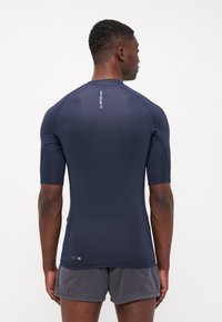Rövid ujjú, sötétkék rash guard, rugalmas anyagból készült, testhezálló fazonú, diszkrét márkázással a hátsó részen.