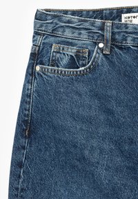 Vaqueros de mezclilla azul de cintura alta con un diseño clásico de cinco bolsillos, costuras visibles y un pequeño detalle en el bolsillo delantero.