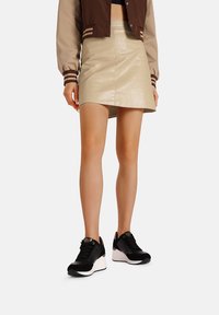 Sneaker in bianco e nero con suola spessa, abbinato a una mini gonna in ecopelle beige e a una giacca bomber marrone e beige.