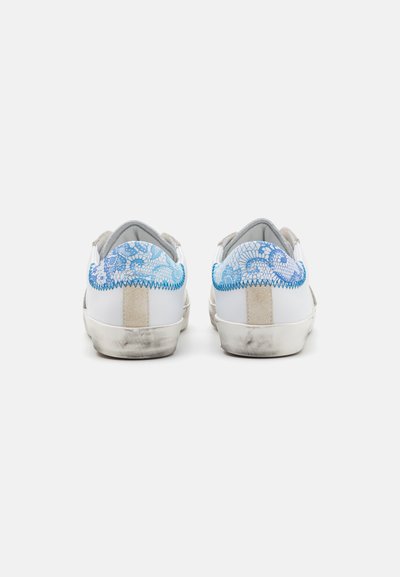 Hvite sneakers med blå snøringdesign bak, semsket aksenter og en litt slitt såle. Rene linjer med en moderne form.