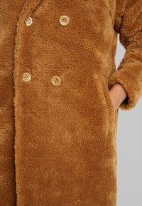 Brun fleecefrakke med en blød tekstur, dobbeltradet design og fire kremfarvede knapper. Har sidelommer og en afslappet pasform.