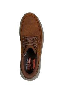 Zapatilla deportiva de cuero marrón con cordones, punta redondeada y superficie texturizada. Cuenta con cuello acolchado y plantilla acolchada con marca visible en el interior.