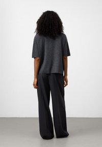 Top grigio a maniche corte con vestibilità ampia e schiena leggermente corta, abbinato a pantaloni grigi a gamba larga, entrambi con texture lisce.