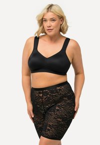 Zwarte stoffen bh met brede banden en een gladde afwerking, gecombineerd met zwarte kanten shorts met bloemmotieven en een rekbare tailleband.