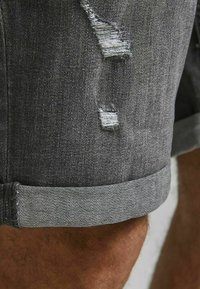 Dark gray denim shorts with a rolled hem, featuring distressed details and frayed patches. Material is soft and textured.