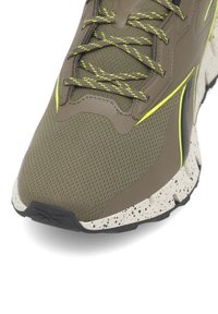Olīvzaļš sporta apavas ar teksturētu acu augšdaļu, kontrastējoši dzelteniem akcentiem un punktiņainu balto zoli. Iekļauj pastiprinātu purngalu.