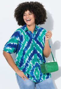 Koszulka z krótkim rękawem z niebiesko-zielonym wzorem tie-dye, w połączeniu z zieloną plecioną torebką. Luźny krój z kołnierzykiem.