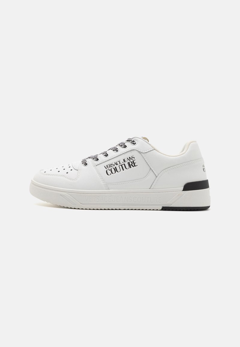 Hvit skinnsneaker med perforert tå, svarte detaljer på sålen og iøynefallende "VERSACE JEANS COUTURE"-merke på siden. Snøring.