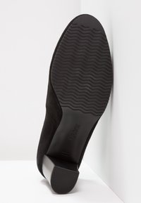 Svart mocka ankle boot med fyrkantig tå, en kraftig häl och en texturerad svart gummisula, med subtil märkning på sulan.