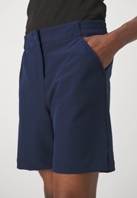 Shorts bleu marine en tissu lisse et léger. Comprend un devant plat, des poches latérales et une taille élastique pour plus de confort.