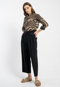 Brązowa i czarna w paski koszula z guzikiem, czarne spodnie plisowane oraz beżowe sandały z kokardką. Gładki materiał i luźny krój.