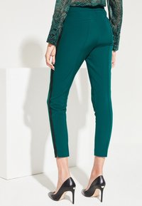 Tegenkleurige, op maat gemaakte broek met een slim fit, voorzien van zwarte zijkanten en een gladde textuur, gecombineerd met zwarte hoge hakken.