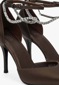 Brown high-heel shoes made of smooth leather, featuring a shiny silver chain accent and a pointed toe design. Black stiletto heel.