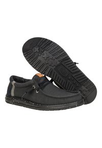 Zapatillas de lona negras con una superficie texturizada, suela de goma con un patrón de estrellas y un acento gris contrastante en el talón. Cierre con cordones.