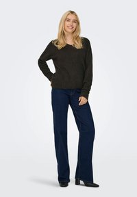 Mørk strikket genser med vid hals, kombinert med vide blå jeans og svarte sko med hæler, vist på en modell. Enkel, uformell påkledning.