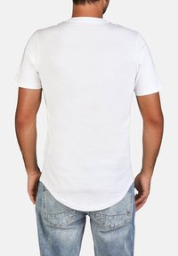 Weißes T-Shirt mit kurzen Ärmeln und abgerundetem Saum, aus weichem Baumwollstoff, getragen mit ausgebleichten blauen Jeans.