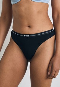 Crne gaćice s bikini krojem, jednostavnog dizajna, elastičnim pojasom s "BOSS" logotipom i kontrastnim bijelim detaljima. Glatka tekstura tkanine.
