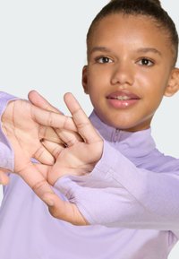 Light purple long-sleeve top with a high collar, featuring fitted cuffs with thumbholes and smooth, stretchy fabric. Model is extending hands.