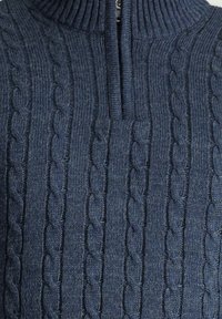 Navyblauer Strickpullover mit hohem Rippkragen, der ein Zopfmuster aufweist und eine halbe Reißverschluss-Front hat. Weicher Stoff.