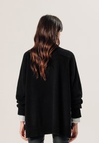 Zwarte oversized sweater van zachte stof. Beschikt over ribgebreide manchetten en zoom, en heeft een relaxte pasvorm. Lange mouwen en minimale details.