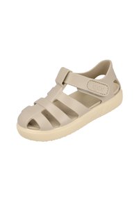 Chancla de goma beige con punta cerrada, lados abiertos y correa ajustable. Suela con textura antideslizante y logo 'igor' en el lateral.