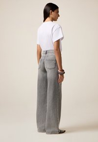 Camiseta blanca de manga corta combinada con unos pantalones grises de cintura alta y pierna ancha, que cuentan con un detalle de botón en el lateral. Textura de tela suave.