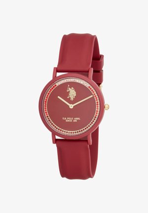 Montre-bracelet rouge U.S. Polo Assn. avec aiguilles dorées, logo joueur de polo, accents de cristaux rouges et roses autour du cadran, et bracelet en silicone.