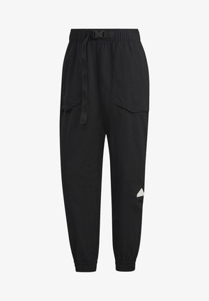 Personne portant un pantalon cargo noir avec des poignets élastiques et des baskets noires, marchant les mains dans les poches.