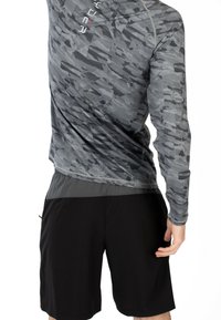 Maglietta sportiva a maniche lunghe di colore grigio con un motivo camouflage testurizzato, abbinata a pantaloni corti neri. Caratterizzata da un materiale traspirante e da un design ergonomico.