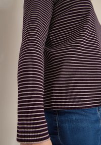 Violetti ja valkoinen raidoitettu ribbipaita pitkillä hihoilla, jossa on muotoon ommeltu malli ja teksturoitu kangas. Yhdistetty sinisiin farkkuihin.