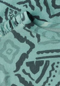 T-shirt en coton vert avec des motifs abstraits sombres, un col rond et une accent froncé sur la couture de l'épaule.