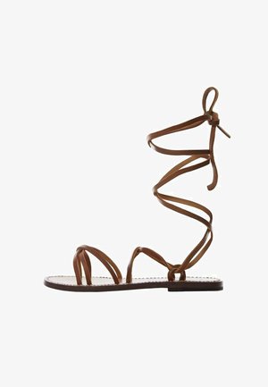 Sandale gladiateur en cuir marron avec de fines lanières en croix et une semelle plate. Une sangle de cheville s'enroule avec un détail en nœud.