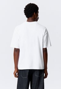 Hvid kortærmet t-shirt med en afslappet pasform og rund hals, lavet af bomuldsstof. Ryggen har et glat, sømløst design.