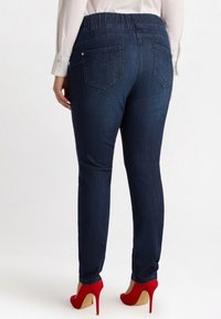Jeans de mezclilla azul oscuro con una cinturilla elástica y dos bolsillos traseros, combinados con zapatos de tacón alto rojos. Textura suave, diseño ajustado.