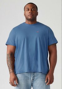 Mėlyna trumpomis rankovėmis medvilninė marškinėlių su apvalia iškirpte, su mažu raudonu Levi's logotipu krūtinėje ir laisvu siluetu. Dėvimi su šviesiais džinsais.