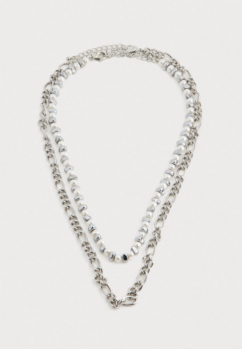 Collier superposé en argent métallique avec des chaînes et des accents de perles blanches, affichant un mélange de finitions lisses et texturées.