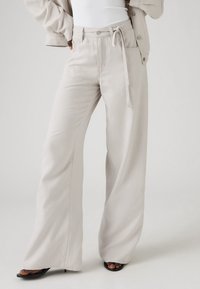 Bež široke hlače od lagane tkanine, s užetom u struku i diskretnim detaljima šavova.