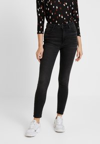 Svarta denim skinny jeans med hög midja, femficka design och subtila blekningar. Kombinerat med en mönstrad svart skjorta och vita sneakers.