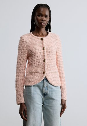 Hele roosa tekstuuriga jope ümmarguse kaelusega, viie kuldse nööbiga ja esitaskutega, kantud helesiniste teksapükste peal.