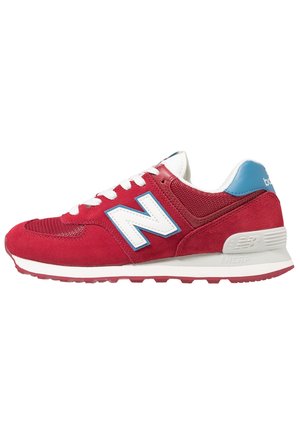 Baskets rouges New Balance avec lacets blancs, languette bleue au talon et logo blanc "N" bordé de bleu, présentées de profil sur fond blanc.