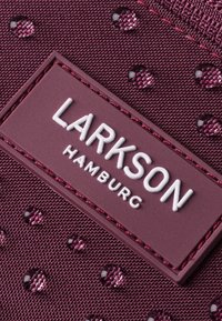 Burgundi szövet, kiemelkedő pöttyökkel, fehér domború "LARKSON HAMBURG" logóval egy téglalap alakú szegmensen, amelyet texturált anyag vesz körül.
