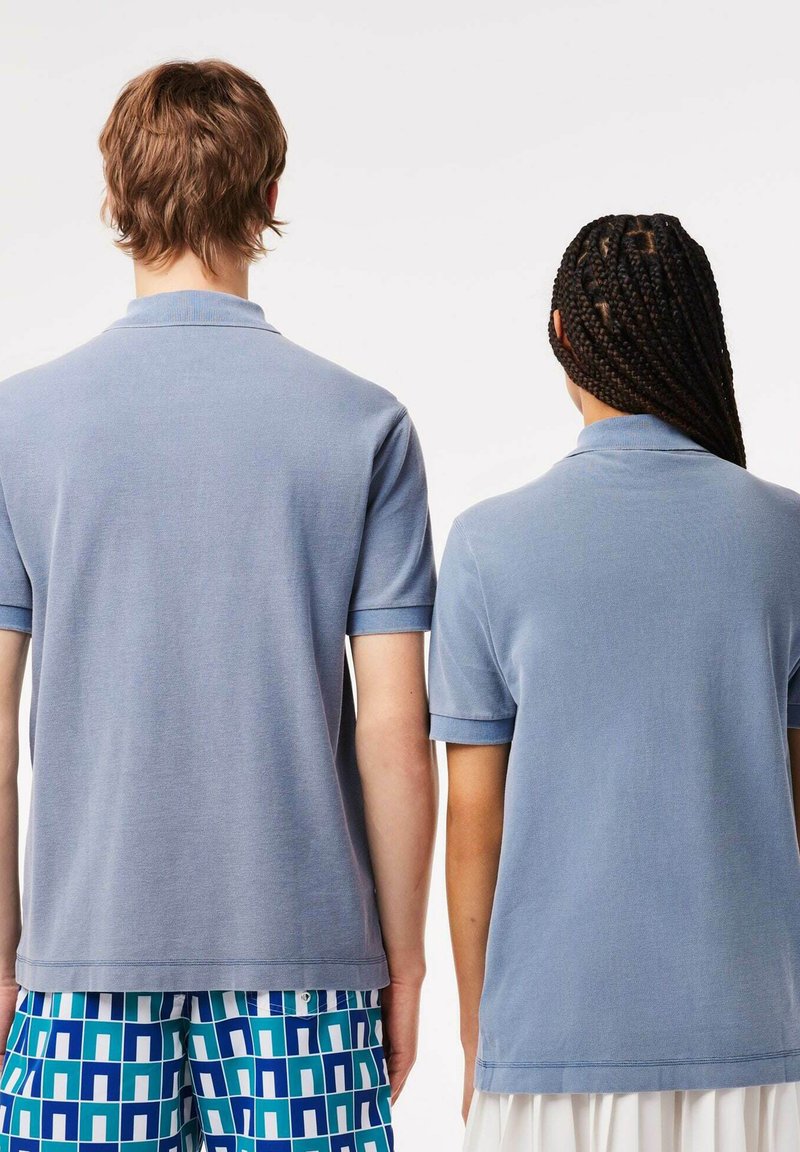 Camisas polo azul claro con cuellos de solapa y mangas cortas, con un tejido texturizado. Una camisa tiene los puños doblados; la otra es lisa.