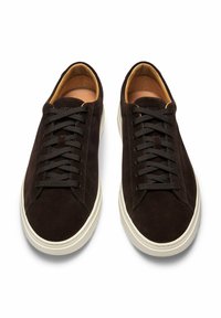 Dunkelbraune Wildledersneaker mit runder Zehenpartie, flacher weißer Sohle und passenden Schnürsenkeln. Das Innenfutter ist beige und verfügt über ein dezentes Markenlabel.