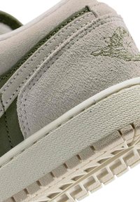 Zamszowy sneaker w jasnoszarym i oliwkowozielonym kolorze, z teksturowanymi akcentami, gumową podeszwą oraz drobnymi detalami przeszyć wzdłuż szwów.