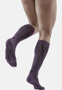 Purple knee-high socks with green horizontal stripes, a ribbed texture, and reinforced toes and heels. Features a size label on the sole.