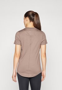 Brun kortärmad träningsöverdel med rundad fåll, sömlös axeldesign och Nike-logga på ryggen i grått. Slät tygtextur.