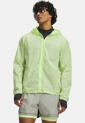 Man wearing neon yellow zip-up hooded jacket, black sunglasses, black long-sleeve top under jacket, and gray shorts with yellow lining.